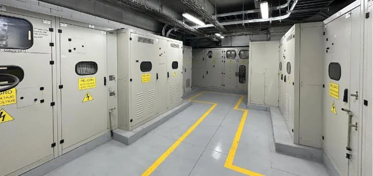 Cuarto de tableros eléctricos con gabinetes industriales y señalización de piso en amarillo.