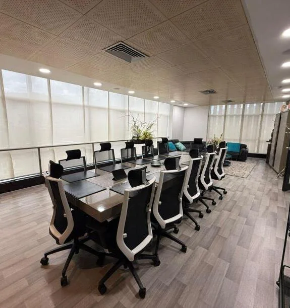 Sala de juntas con mesa alargada, sillas negras y blancas, y cortinas translúcidas frente a los ventanales.