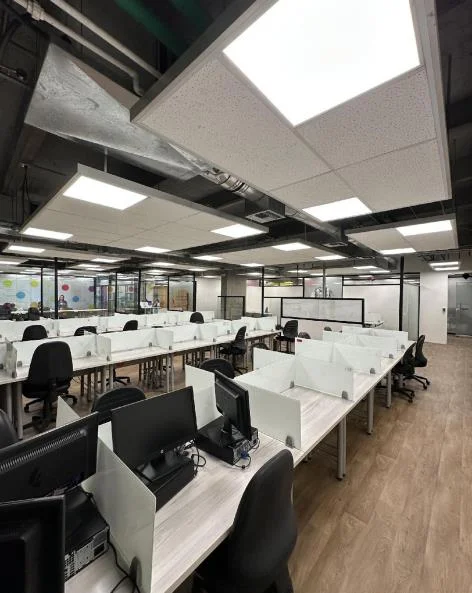 Corredor de oficinas con paredes de vidrio, mesas y sillas dispuestas en perspectiva hacia el fondo del piso.