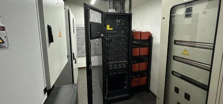 Cuarto de UPS con gabinete abierto que muestra baterías de respaldo y señalización de riesgo eléctrico.