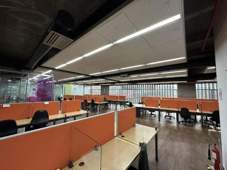 Piso de oficinas con divisores color naranja, columnas estructurales a la vista y techo industrial.