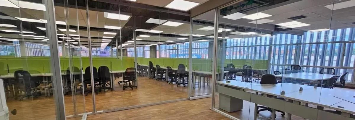 Piso de oficinas vacío con divisiones de vidrio, iluminación LED en el techo y vista a la ciudad a través de las persianas exteriores.